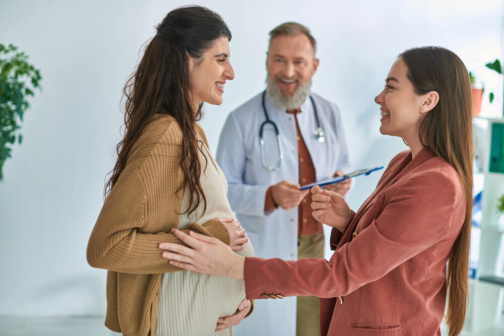 cheerful gynecologist looking at pregnant woman with her partner, in vitro fertilizing concept